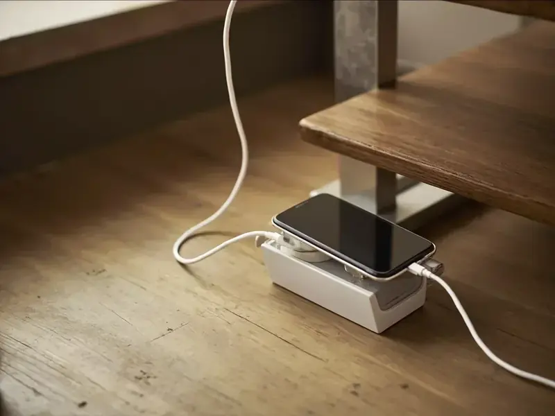 A charging cable and face-down phone beside a low teak table