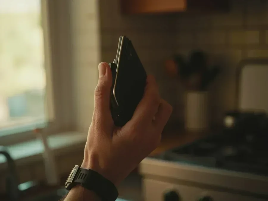A hand holding a dark handset in a kitchen, screen unreadable