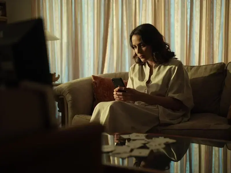A woman on a sofa testing a phone beside a discard pile